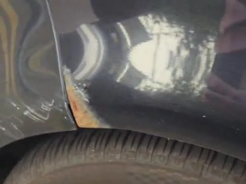A dark car's rear quarter panel, with rust and flaking paint at the trailing edge of the wheel arch, above the tyre.